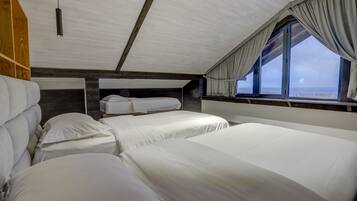 Una cabaña con tres camas, paredes de madera y un ventanal con cortinas.