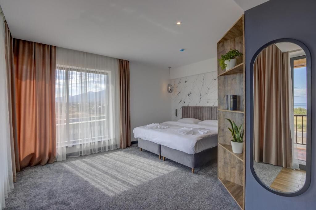 Una habitación de hotel moderna con una cama grande, un estante empotrado con plantas y vistas a través de la ventana.