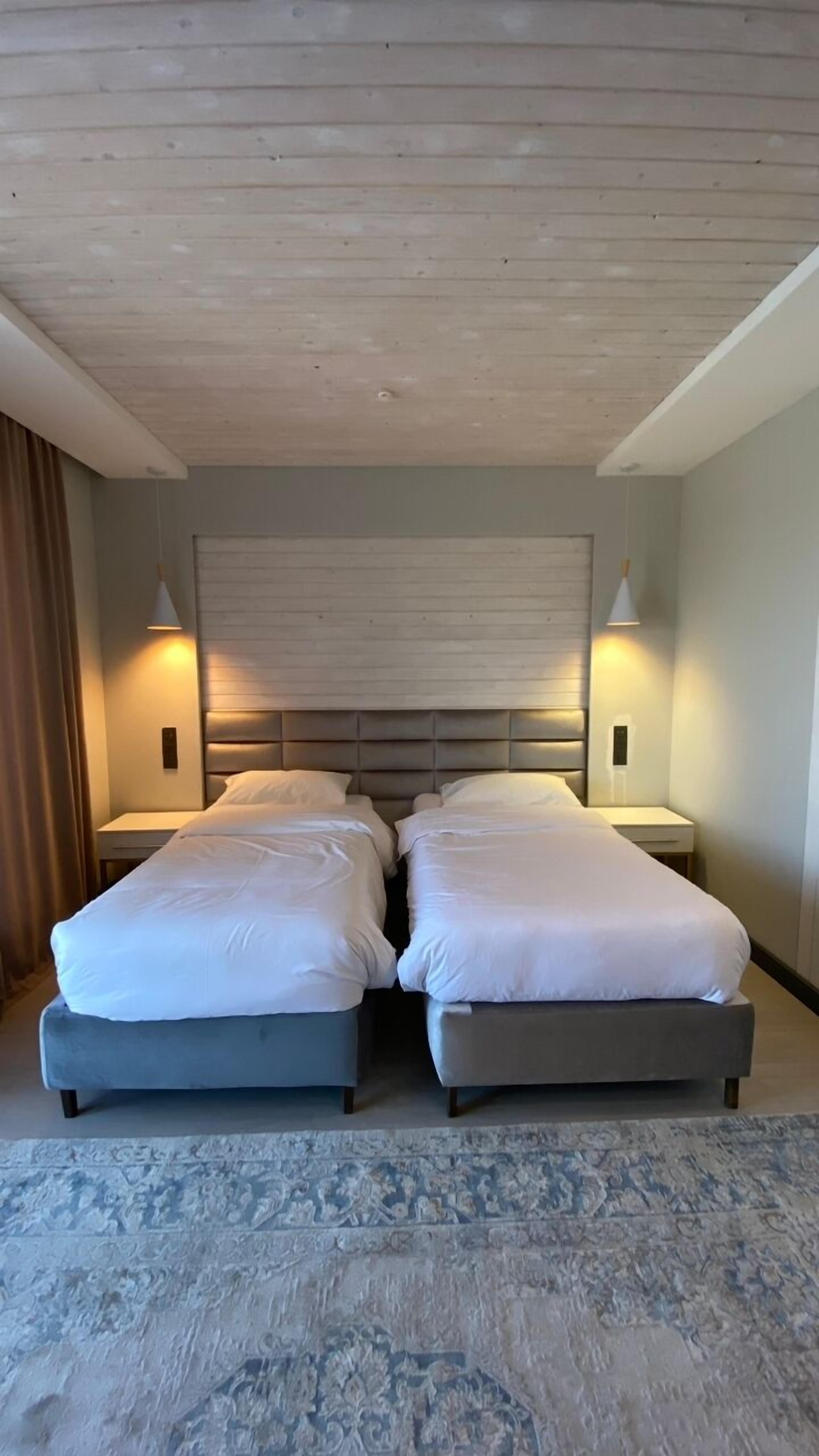 A hotel room with two beds, a wooden ceiling, and a patterned rug.