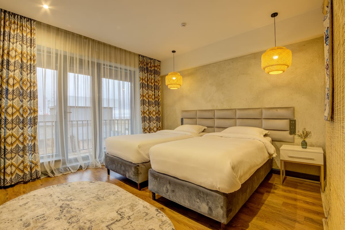 A bedroom with two beds, a large window with sheer curtains, and a patterned rug.