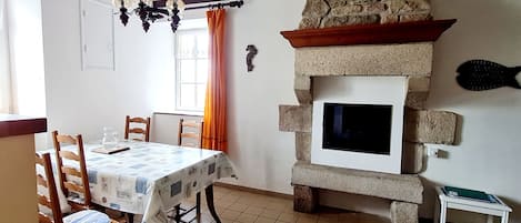 A dining area with a table set for two, a stone fireplace, and a window with curtains.