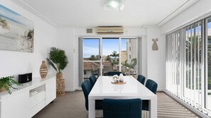 Uma sala de jantar moderna com uma mesa branca, cadeiras azuis e vista para edifícios através de janelas amplas.