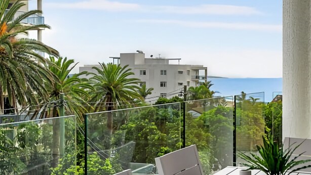 Un balcon avec des garde-corps en verre, un ordinateur portable et une vue sur un immeuble et la mer.
