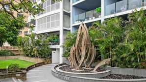 Un bâtiment moderne, orné d’une sculpture centrale, entouré d’une végétation luxuriante et d’une pelouse bien entretenue.