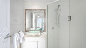 Casa de banho moderna com lavatório de vidro, chuveiro e espelho com moldura de mosaico.