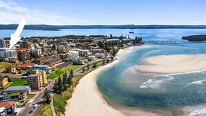 Vue aérienne d’une ville côtière avec une plage, des immeubles résidentiels et une jetée qui s’avance dans l’eau.