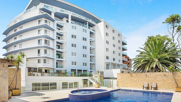 Um hotel moderno de vários andares com área de piscina, incluindo uma banheira de hidromassagem e uma escadaria que leva aos andares superiores.