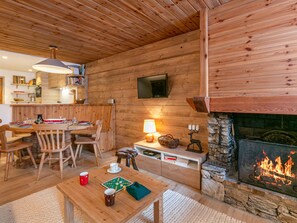 L’intérieur d’un chalet confortable, avec une salle à manger, une cheminée et un téléviseur fixé au mur.