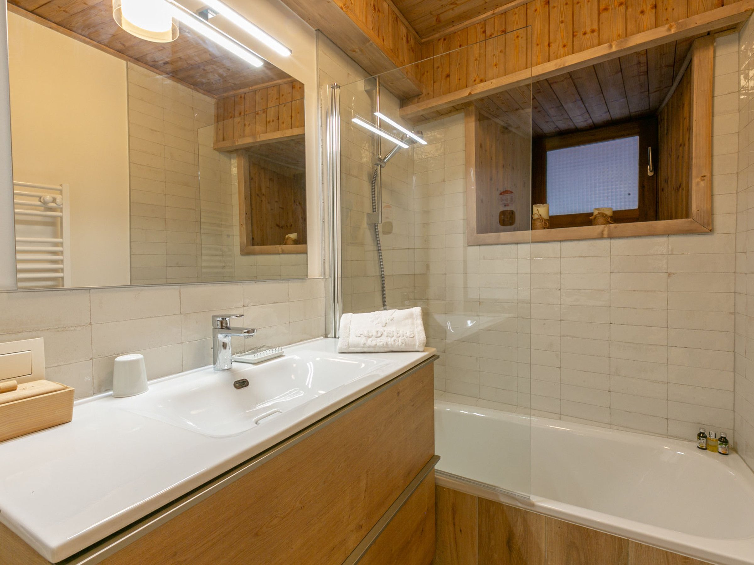Een moderne badkamer met een houten wastafel, een grote spiegel, een bad en een douche.