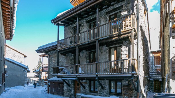 Ein Steinhaus mit einem hölzernen Balkon und verschneitem Grund.