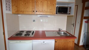 A compact kitchen with wooden cabinets, a microwave, a stove, and a dishwasher. - 6-person apartment in Chamrousse, south-facing, 2 bedrooms (Chamrousse)