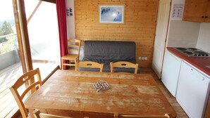 A compact kitchen with wooden walls, a dining table with chairs, a small refrigerator, and a stove. - 6-person apartment in Chamrousse, south-facing, 2 bedrooms (Chamrousse)