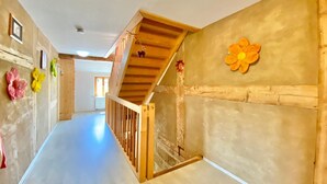 Un pasillo con una escalera de madera, una decoración floral en la pared y vista a otra habitación.