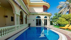 A swimming pool with a curved edge, a covered patio area with a railing, and a palm tree in the background. - Sparking signature Beach front villa reverera mediterian style in Palm Jumeirah  (Dubai)
