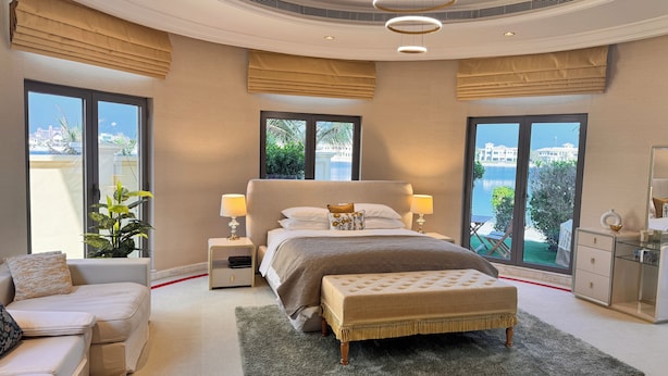 A modern bedroom with a large bed, two bedside tables, a bench, a sofa, and large windows offering a view of the sea. - Sparking signature Beach front villa reverera mediterian style in Palm Jumeirah  (Dubai)
