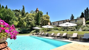 A swimming pool with lounge chairs and umbrellas, surrounded by greenery and a building with a tower. - Exlusive luxury villa with private pool in the heart of Tuscany (Linari)