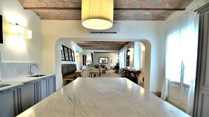 A spacious kitchen with a marble island, wooden beams on the ceiling, and a large window on the right. - Exlusive luxury villa with private pool in the heart of Tuscany (Linari)