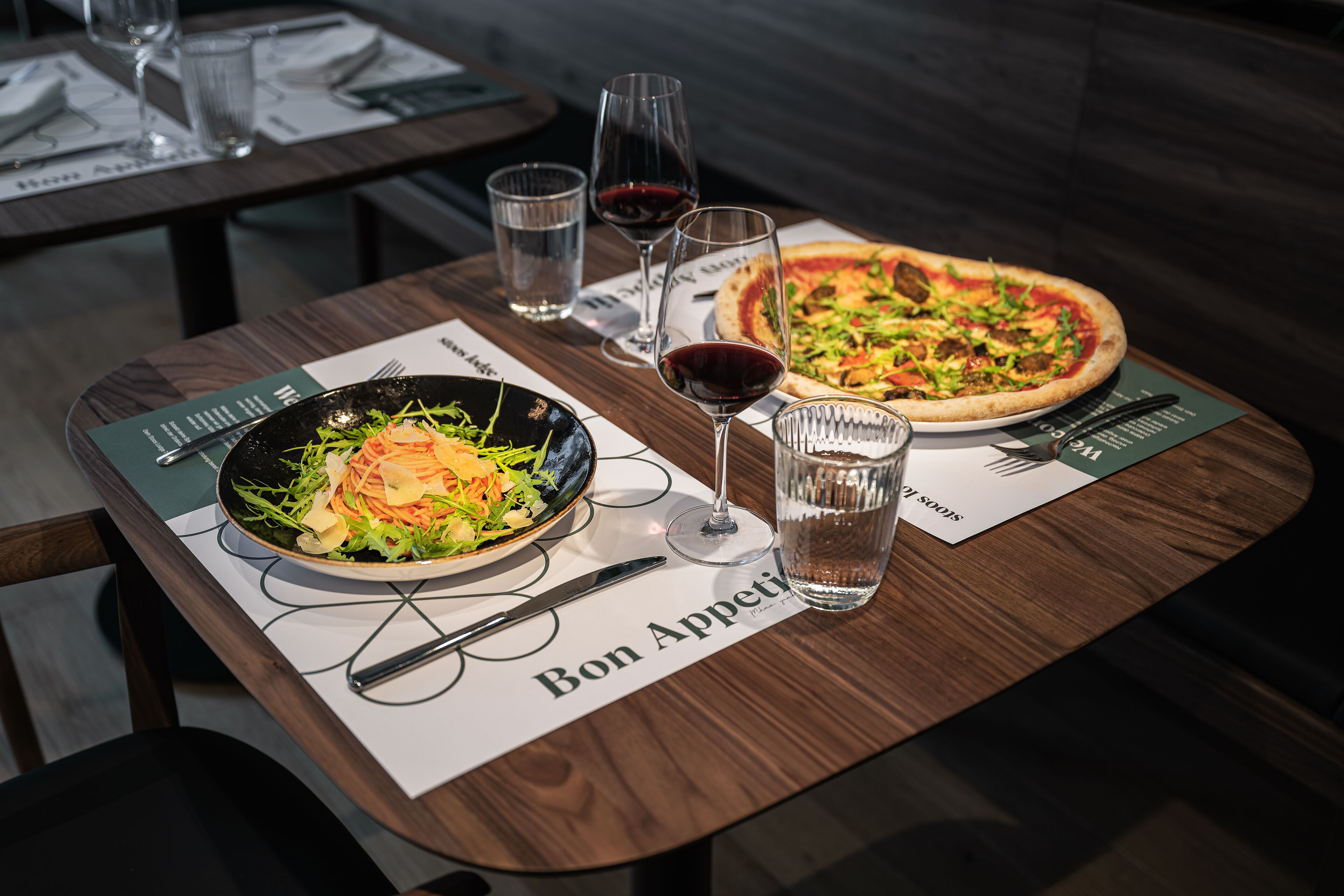 A dining table with a salad, a pizza, and two glasses of red wine.