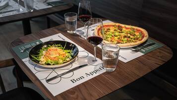 A dining table with a salad, a pizza, and two glasses of red wine.