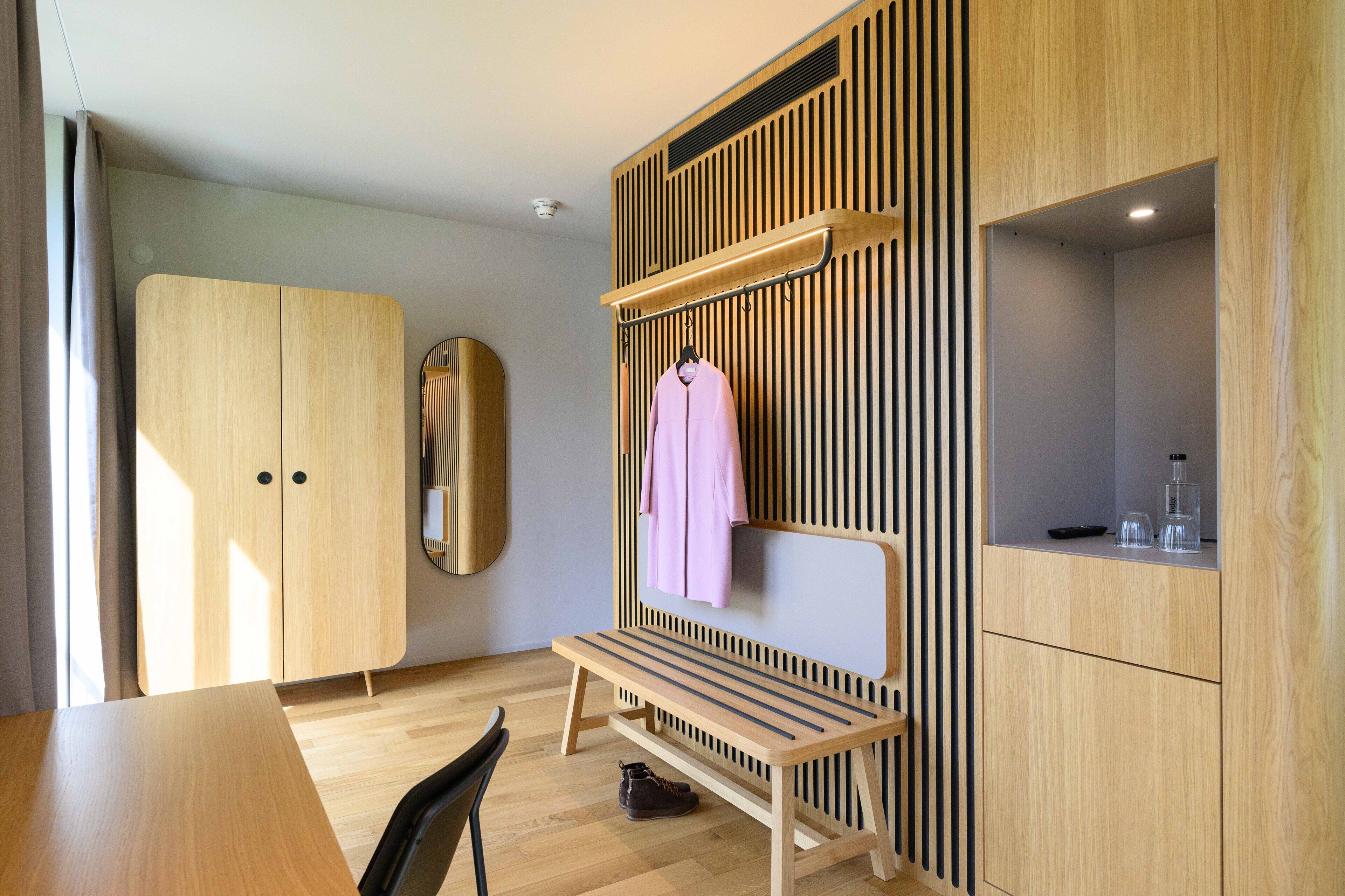 Une chambre moderne avec une armoire en bois, un banc et un miroir.