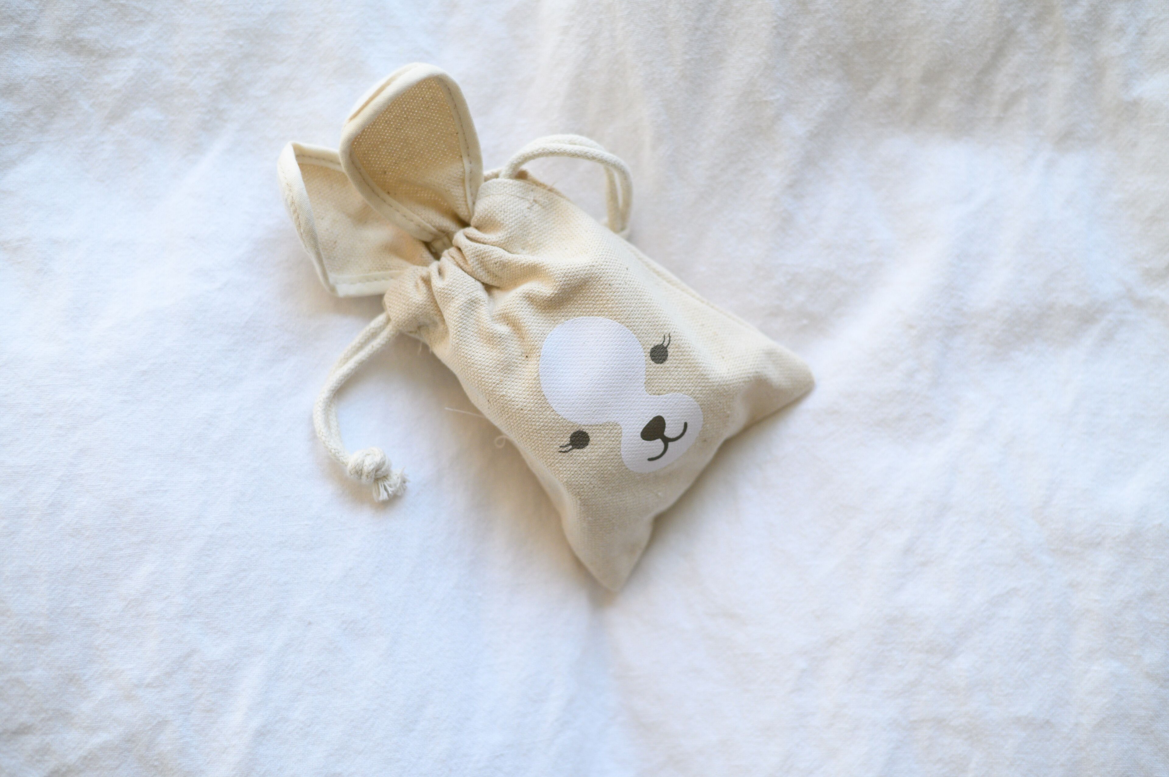 Una pequeña bolsa de cordón con un diseño de conejito sobre un fondo de tela blanca.