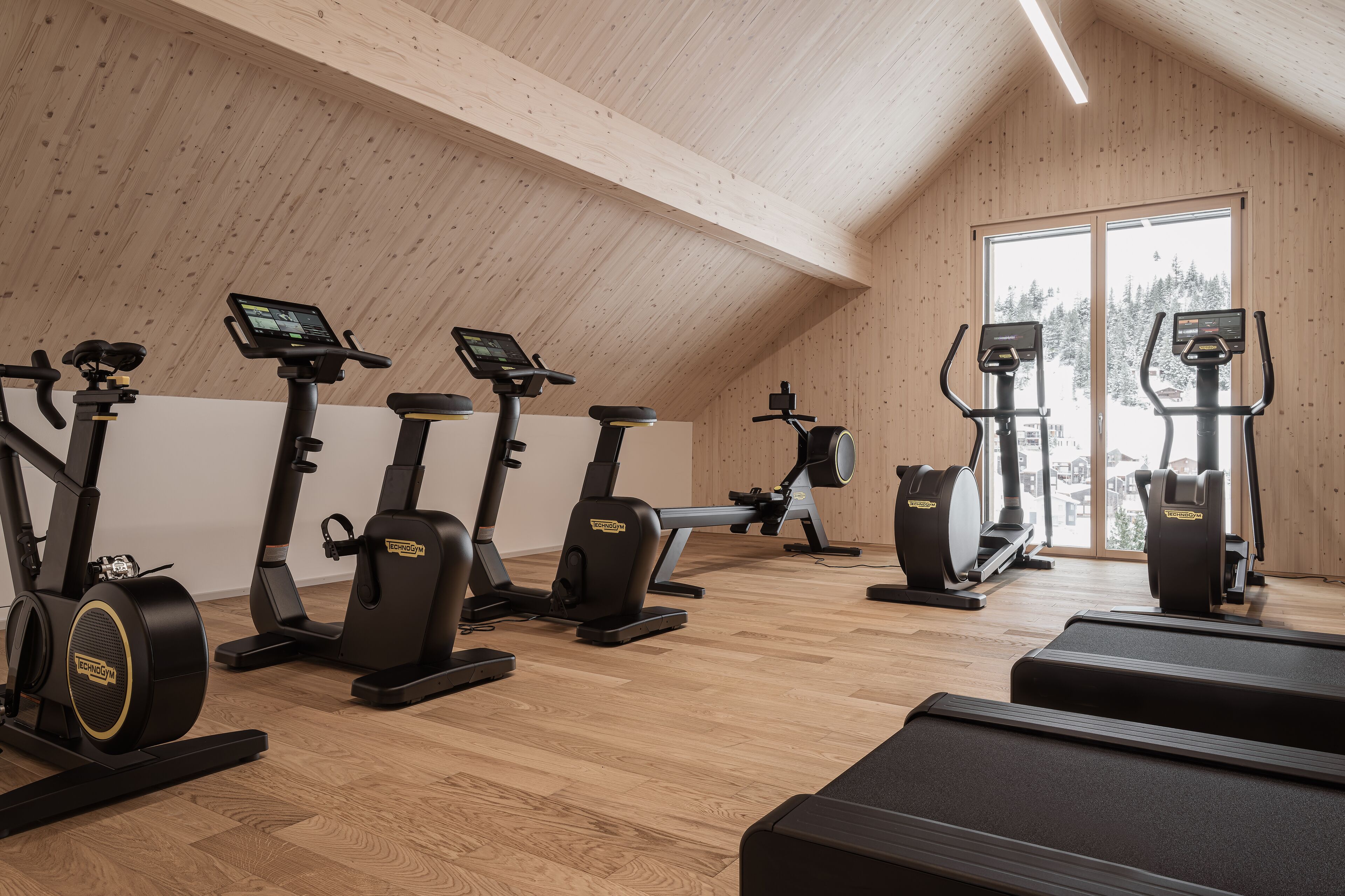 A gym with multiple exercise machines, wooden walls, and a large window.