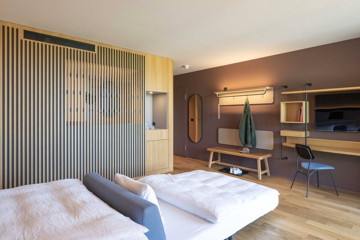 Moderni hotellihuone, jossa on kaksi sänkyä, puusäleseinä, peili, televisio, penkki ja tuoli.