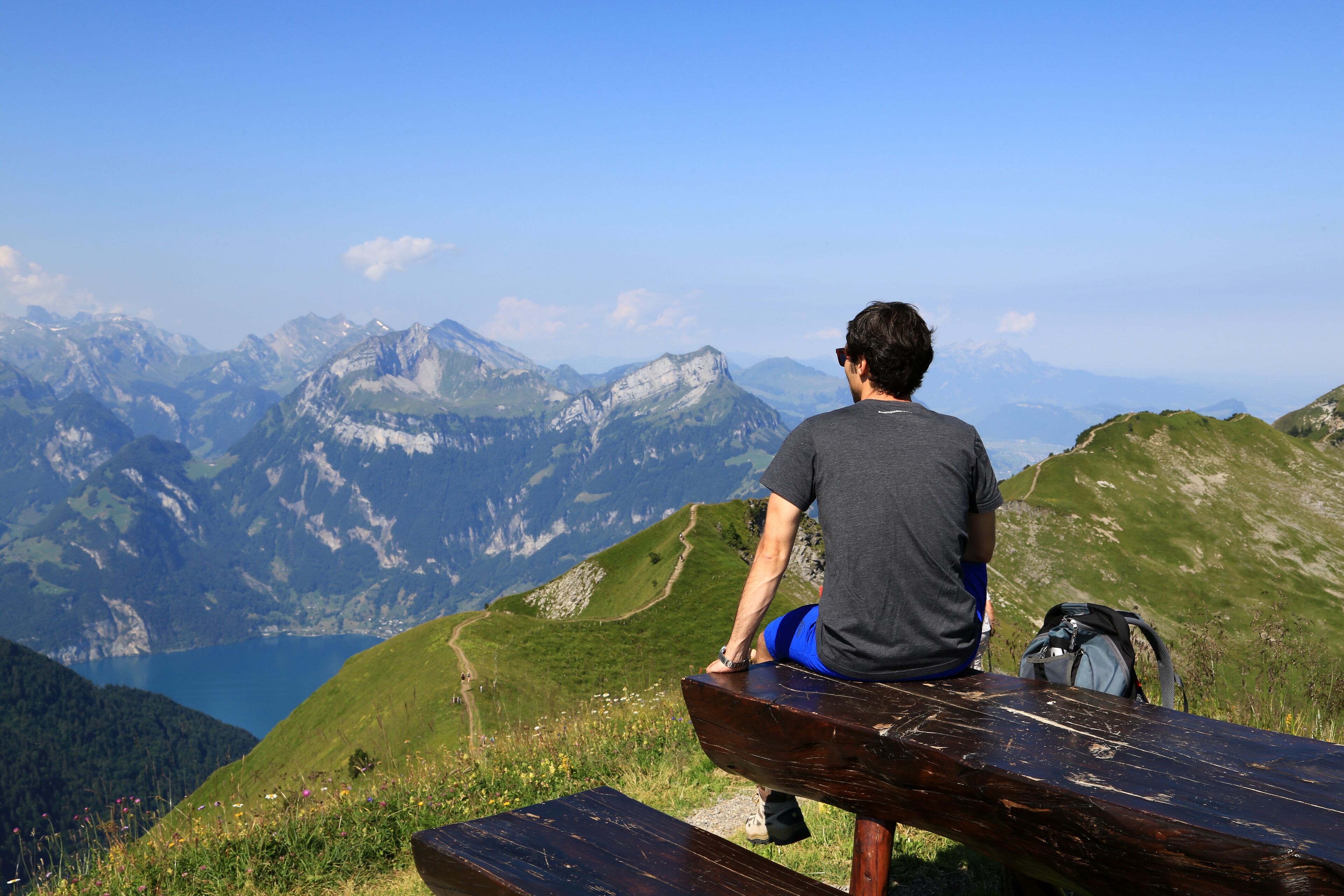 A person sitting on a bench overlooking a mountainous landscape with a lake and a clear sky.