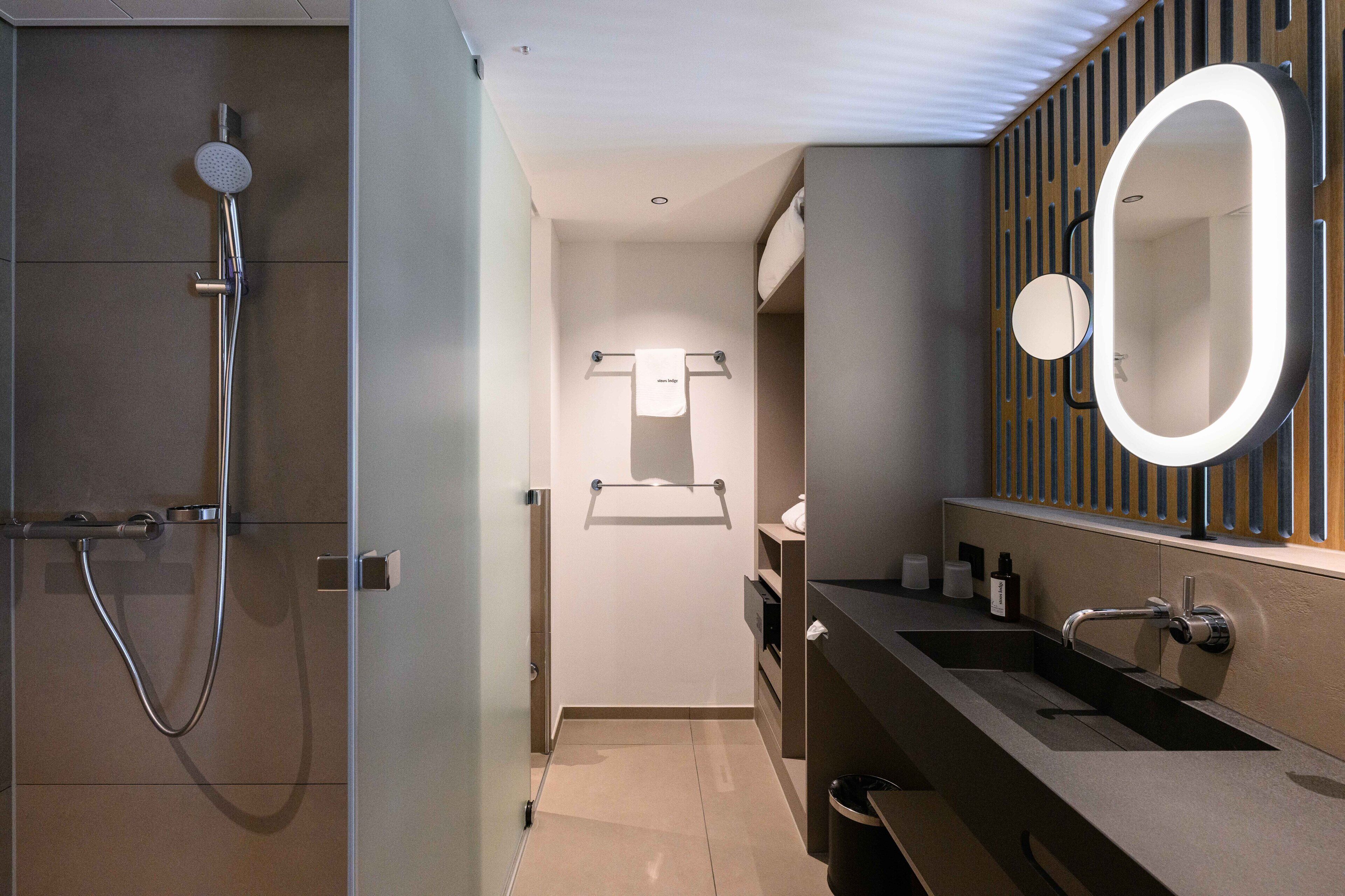 Un baño moderno con ducha, tocador con espejo y un perchero para toallas.