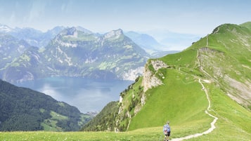 A hiker on a mountain trail with a lake and mountains in the background.