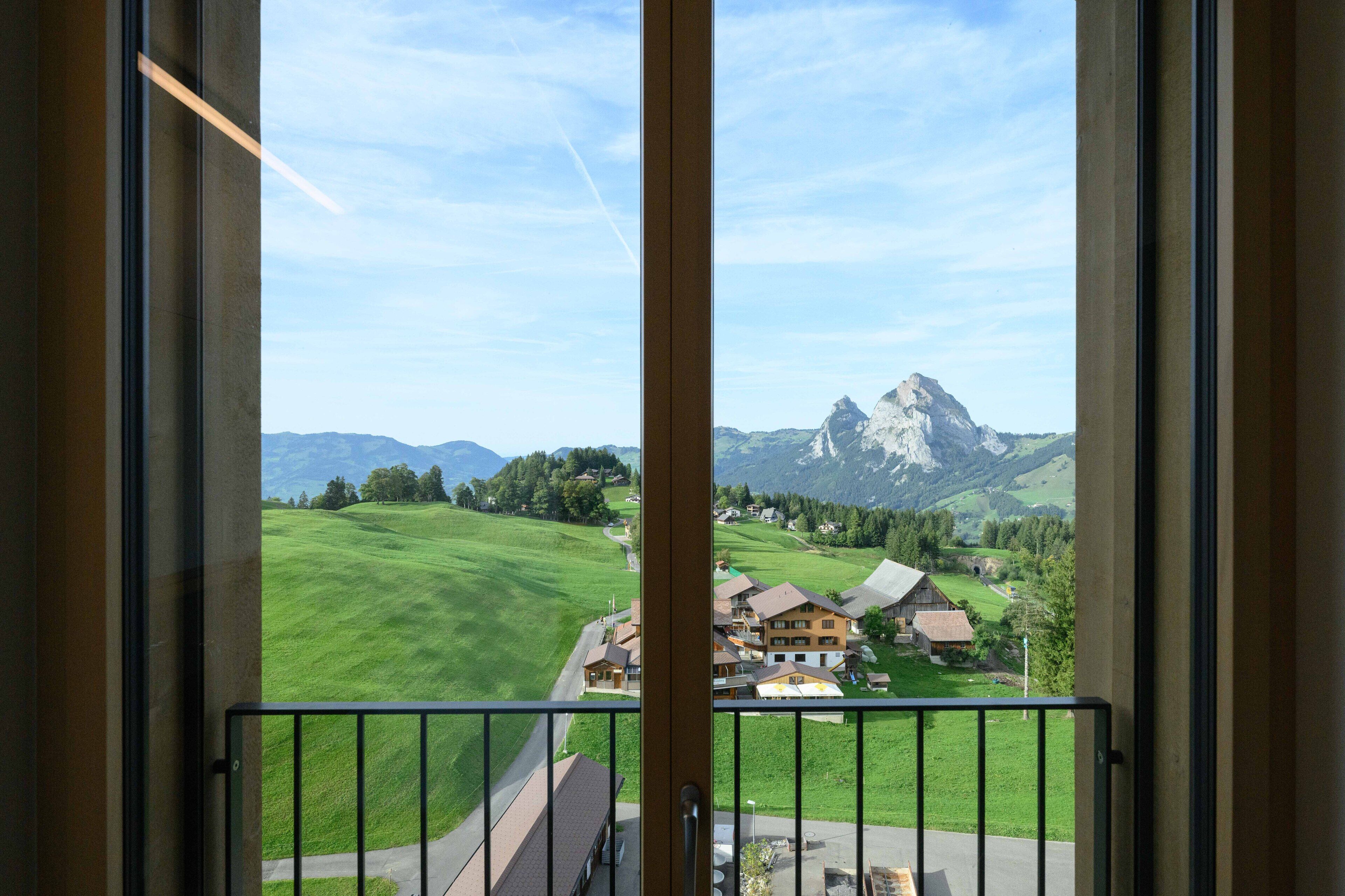A balcony with a view of a green valley, a mountain, and a small village.