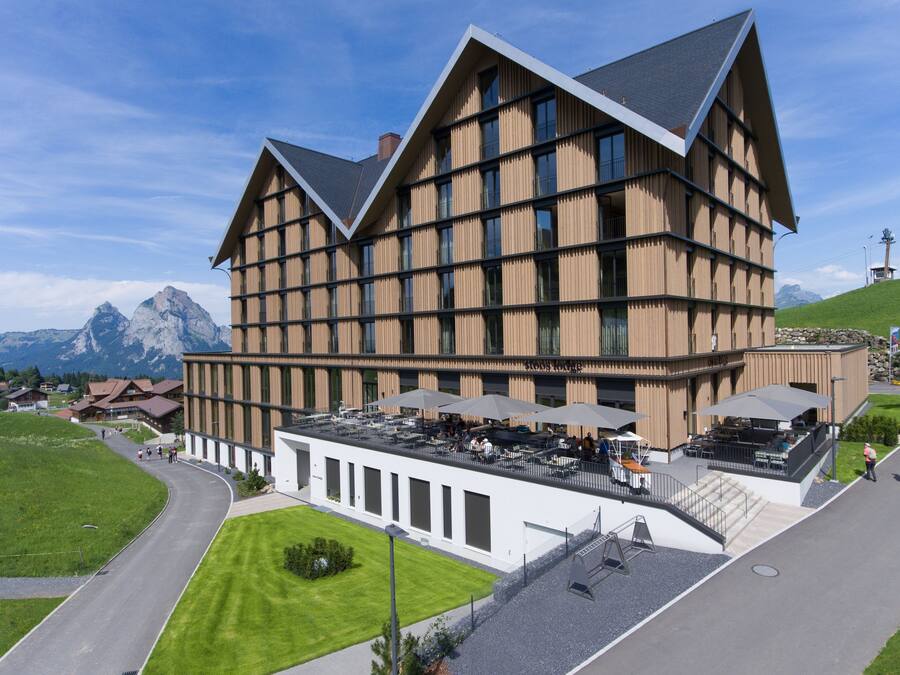 A modern building with a sloped roof, large windows, and a terrace with outdoor seating.