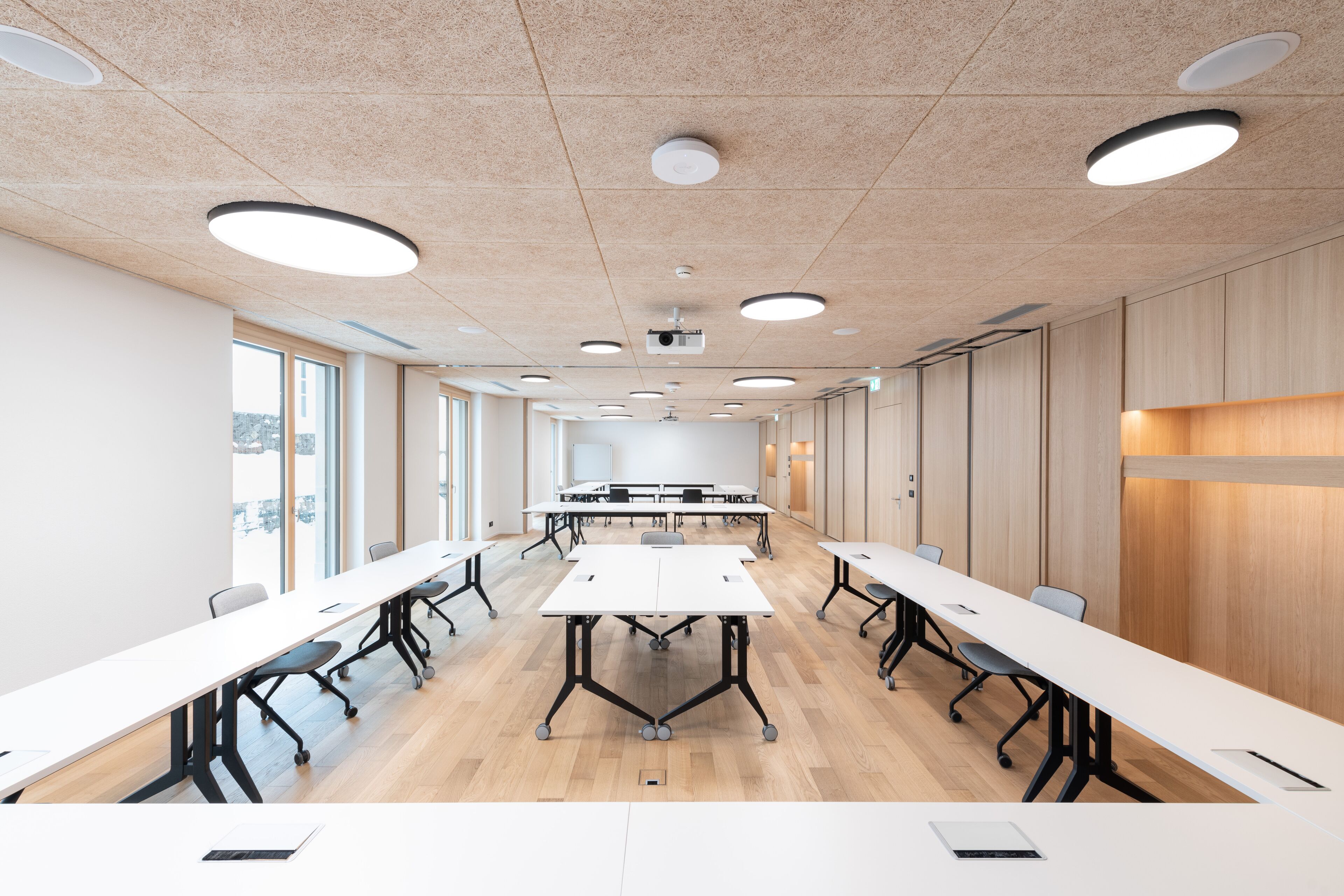 A conference room with long tables, white walls, wooden paneling, and ceiling lights.