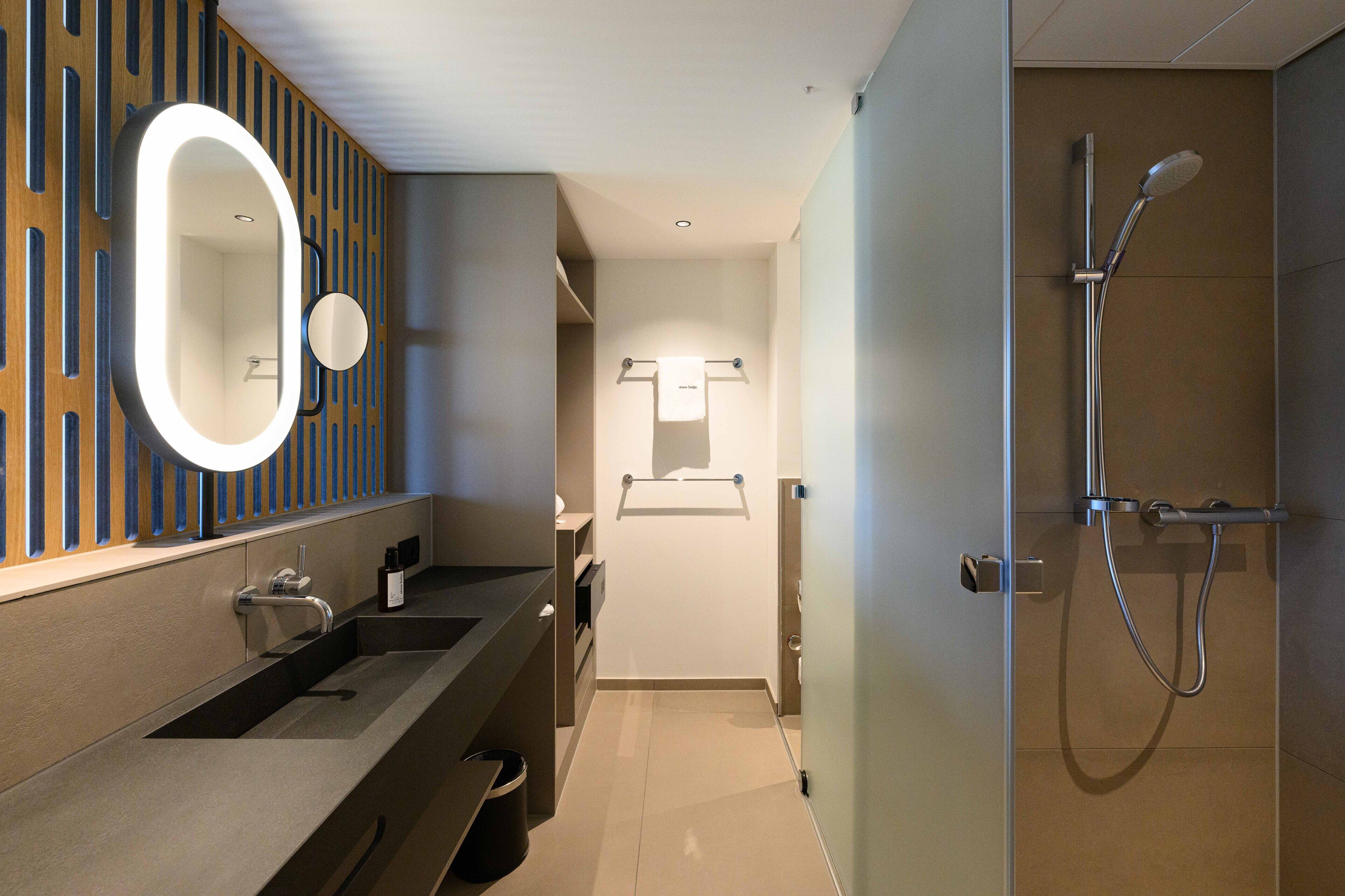 Een moderne badkamer met een grote spiegel, een douche en een wastafelmeubel met een wastafel.