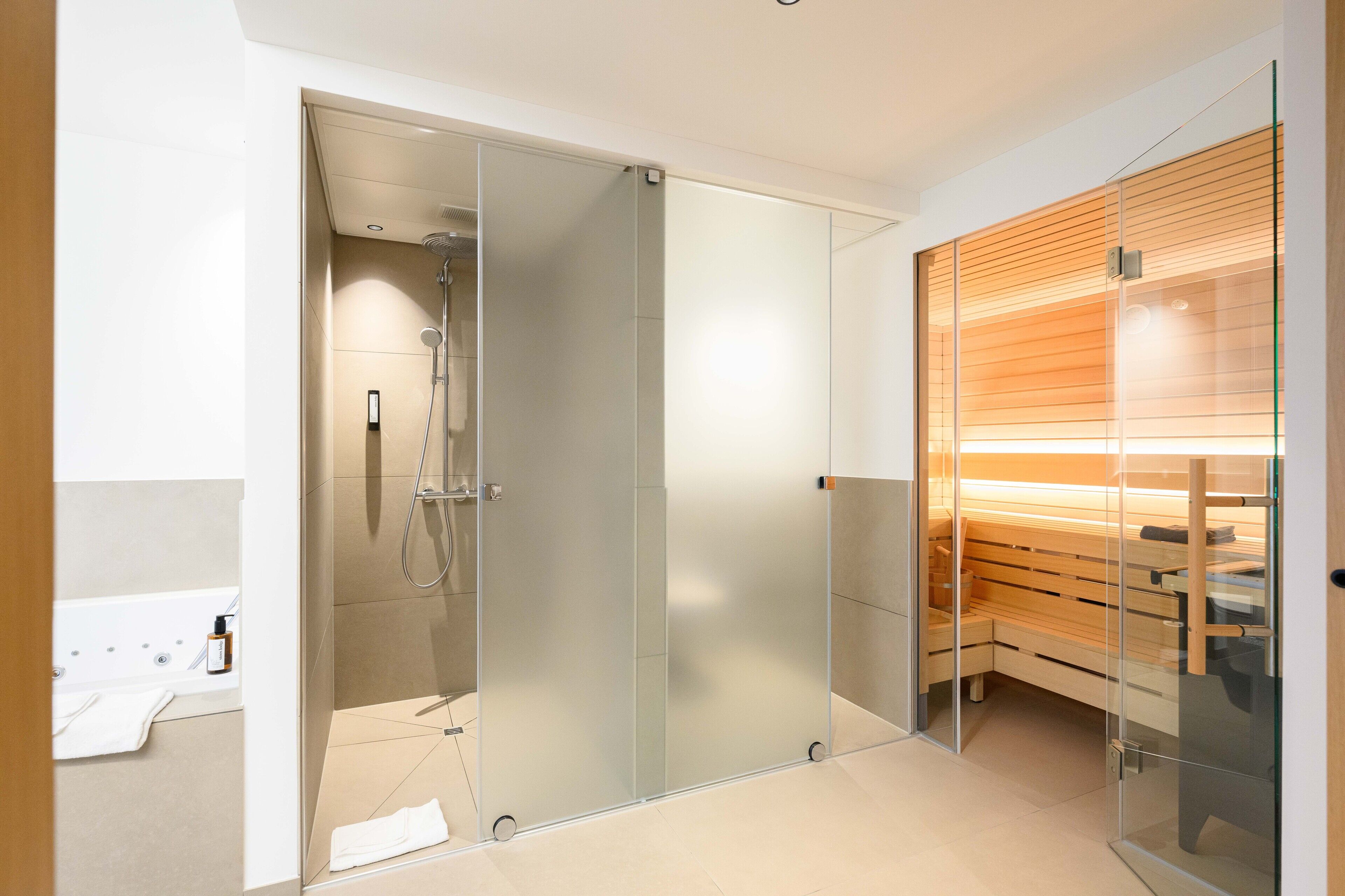 A modern bathroom with a glass shower enclosure, a wooden bench, and a white bathtub.