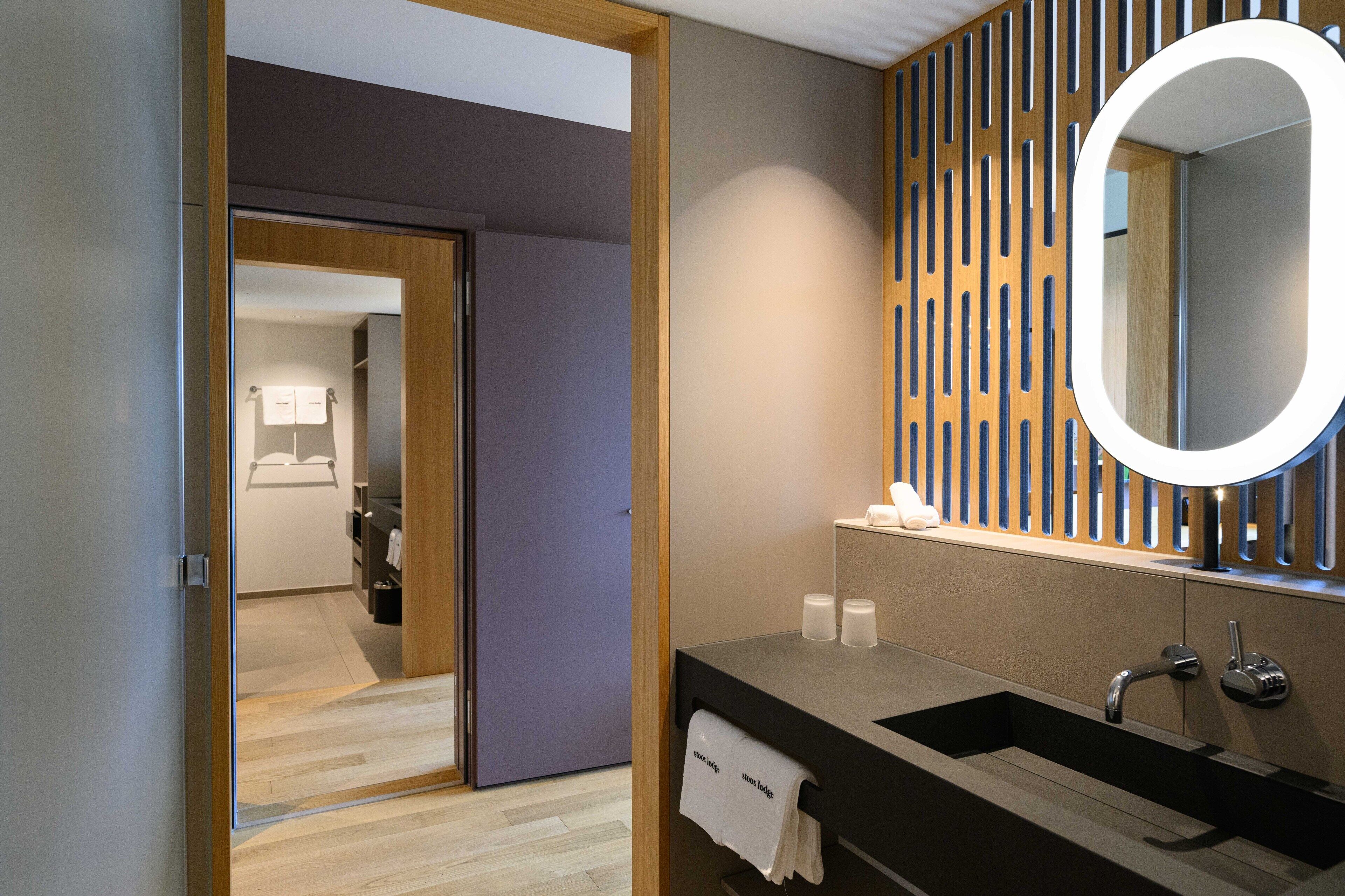 Un baño moderno con un espejo grande, un lavabo negro y un diseño de paneles de madera en la pared.