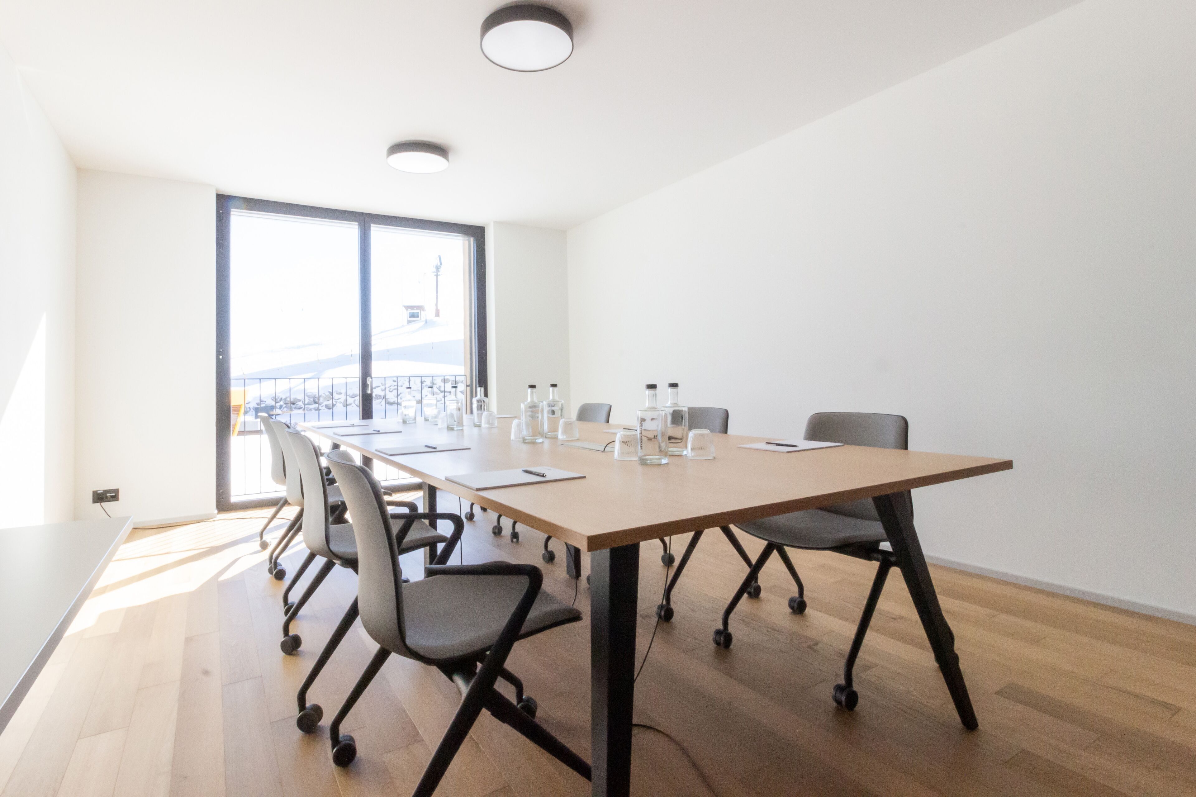 A conference room with a long table, chairs, and a view through a large window.