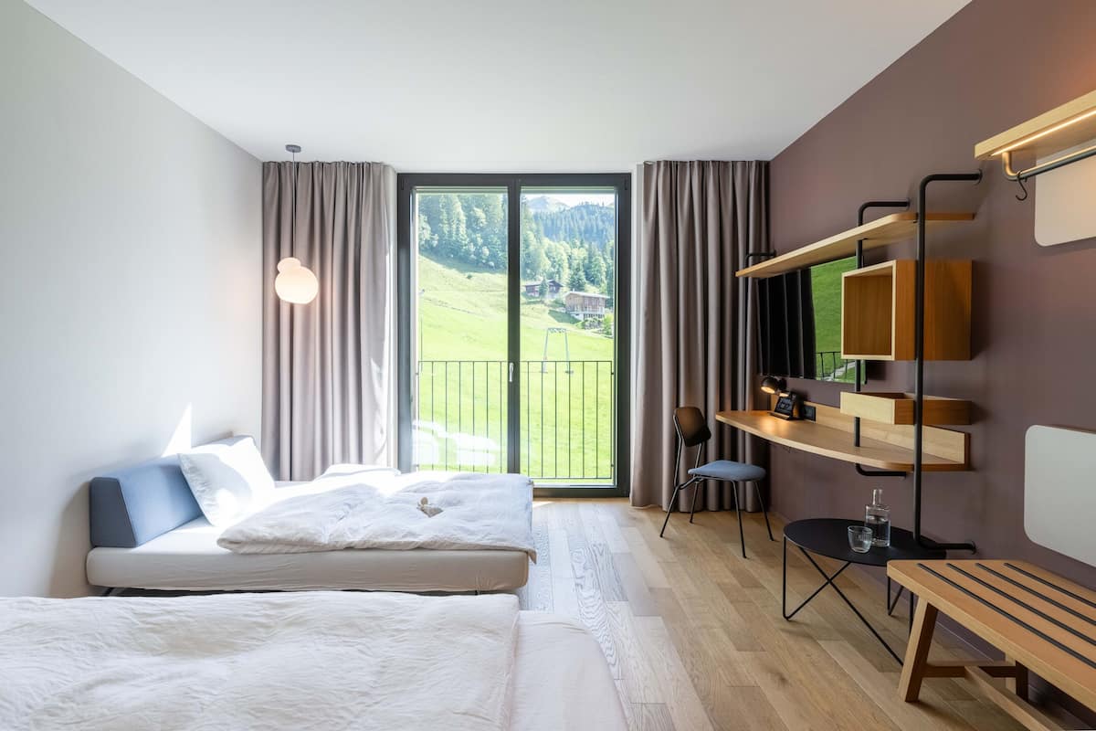 Moderni hotellihuone, jossa on suuri ikkuna, sänky, työpöytä ja tuoli.