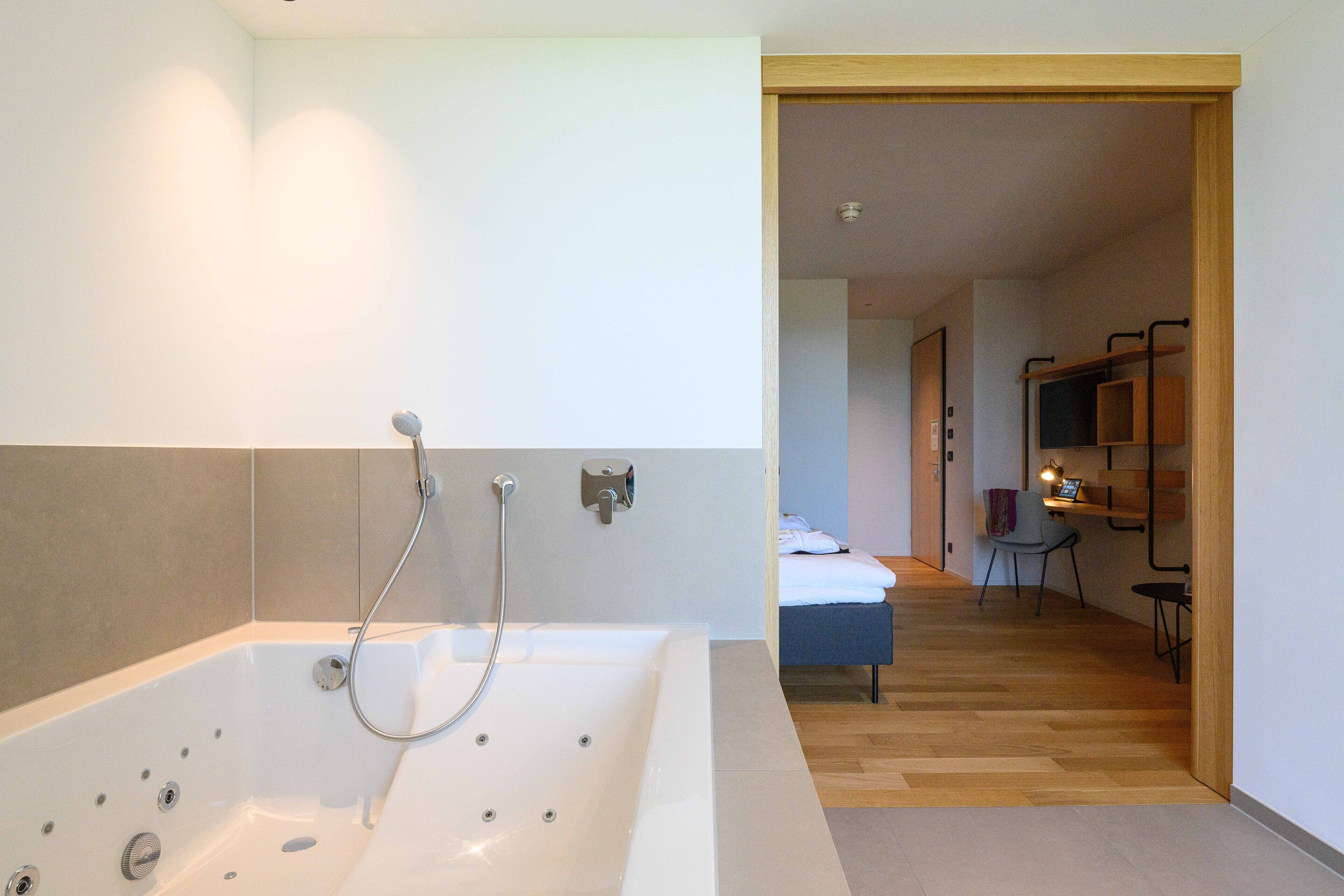 Une salle de bain moderne dotée d’une grande baignoire, d’une douche et d’un plancher en bois menant à une chambre à coucher avec un lit et un bureau.