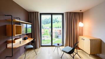 Una habitación de hotel moderna con un ventanal grande, un escritorio con silla, una mesita y un armario.