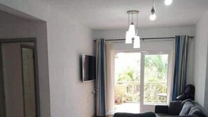 A modern living room with a sectional sofa, a TV mounted on the wall, and a dining area with a table and chairs. - La Marquise Apartment with pool (Flic en Flac)