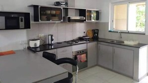 A compact kitchen with a gas stove, microwave, and a window providing natural light. - La Marquise Apartment with pool (Flic en Flac)