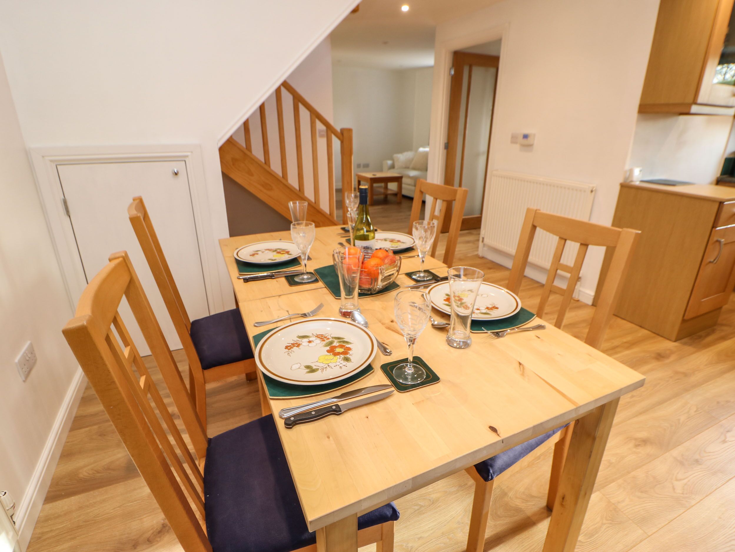 Un comedor con una mesa de madera dispuesta para cuatro personas, incluyendo platos, cubiertos y vasos.