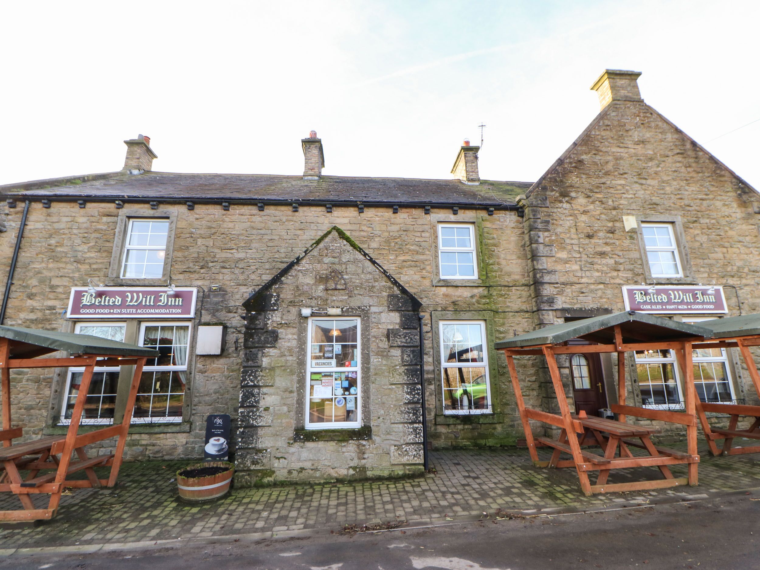 A traditional stone building with two signs reading "Belted Will Inn" and a window displaying various items.