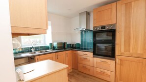 A modern kitchen with wooden cabinets, a black oven, and a teal backsplash. - Stable Cottage (Brampton)