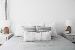 A bed with white bedding and two nightstands on either side, each with a lamp and a small clock.