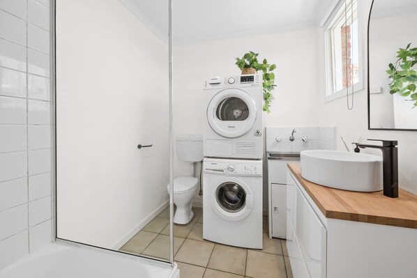A modern bathroom with a stacked washer and dryer, a toilet, a sink, and a mirror.