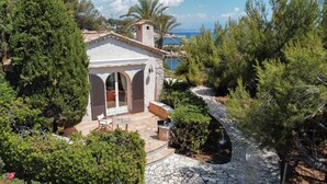 Una villa con un camino de piedra que conduce a un porche cubierto, rodeada de exuberante vegetación y con vistas a la costa.