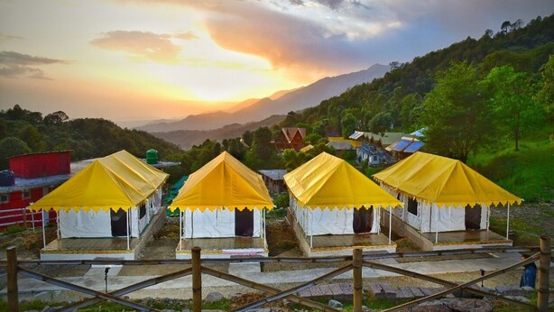 A row of yellow and white tents with a mountainous backdrop. - Parker Camps (Baijnath)