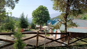 A rustic wooden gate leading to a rural area with a small building and a large tree in the background. - Parker Camps (Baijnath)